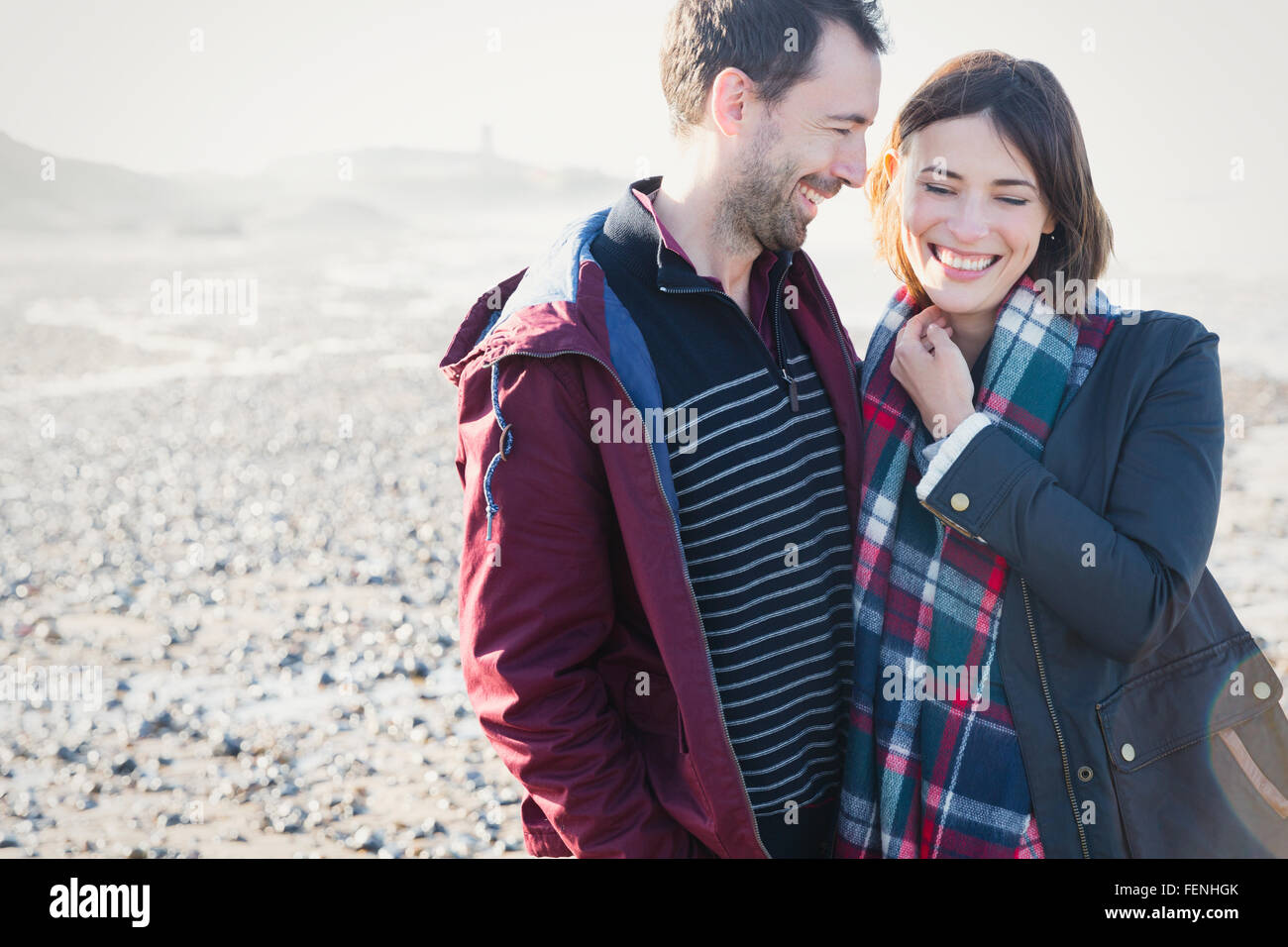 Smiling brunette couple standing on sunny rocky beach Stock Photo