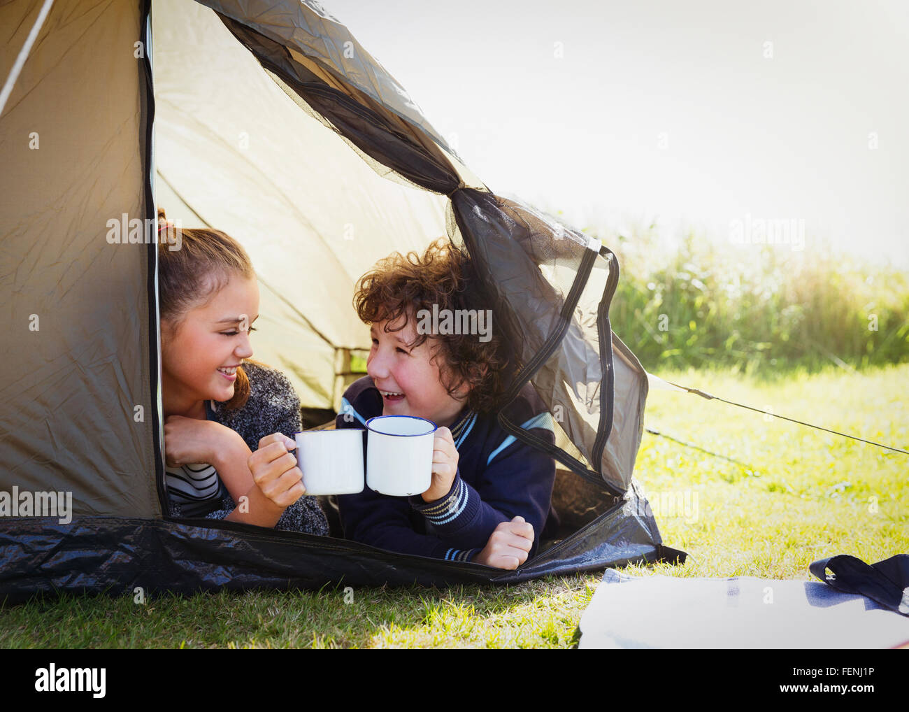 Brother and sister toasting mugs in tent Stock Photo