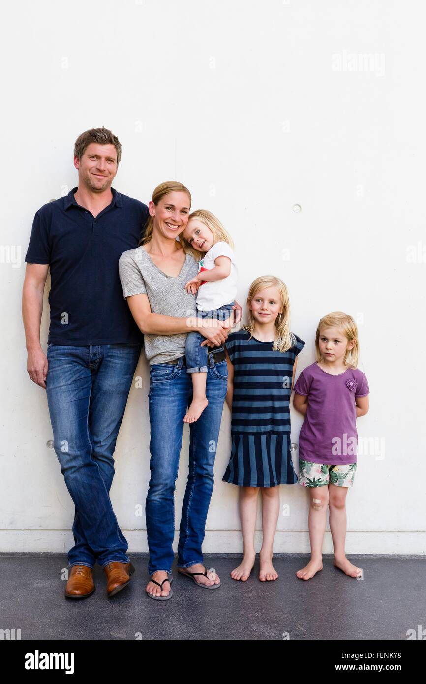 Portrait of parents and three young daughters standing in front of white wall Stock Photo