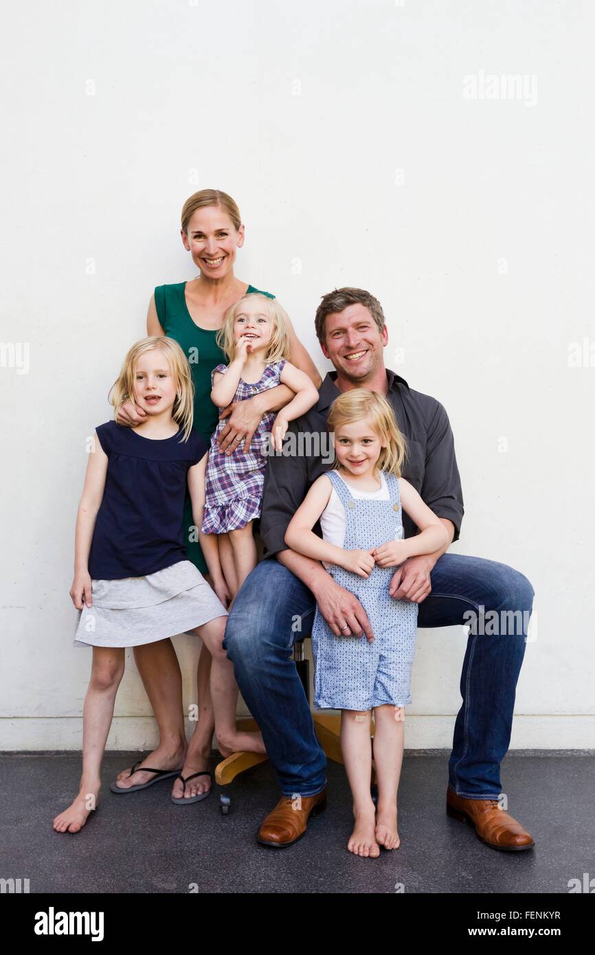 Family portrait of parents and three young daughters in front of white wall Stock Photo
