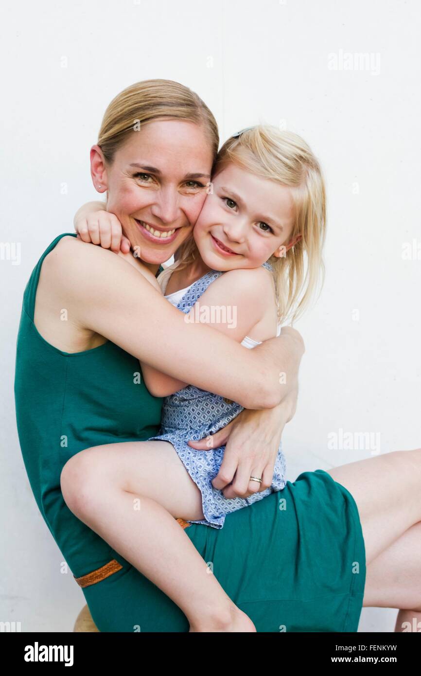 Portrait of mid adult woman with daughter sitting on lap in front of white wall Stock Photo