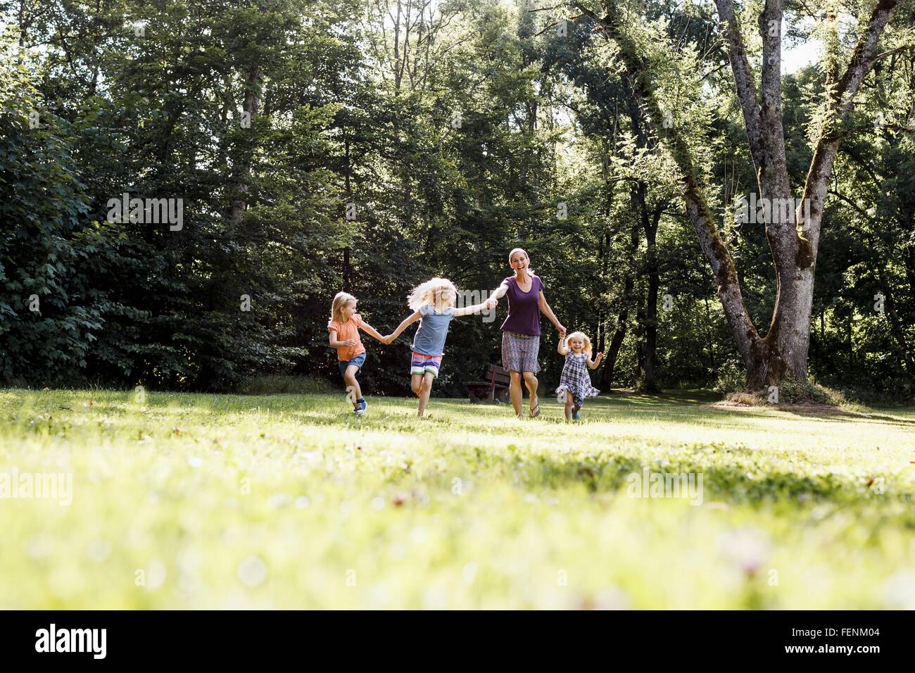 Mid adult woman and three young daughters holding hands and running in park Stock Photo