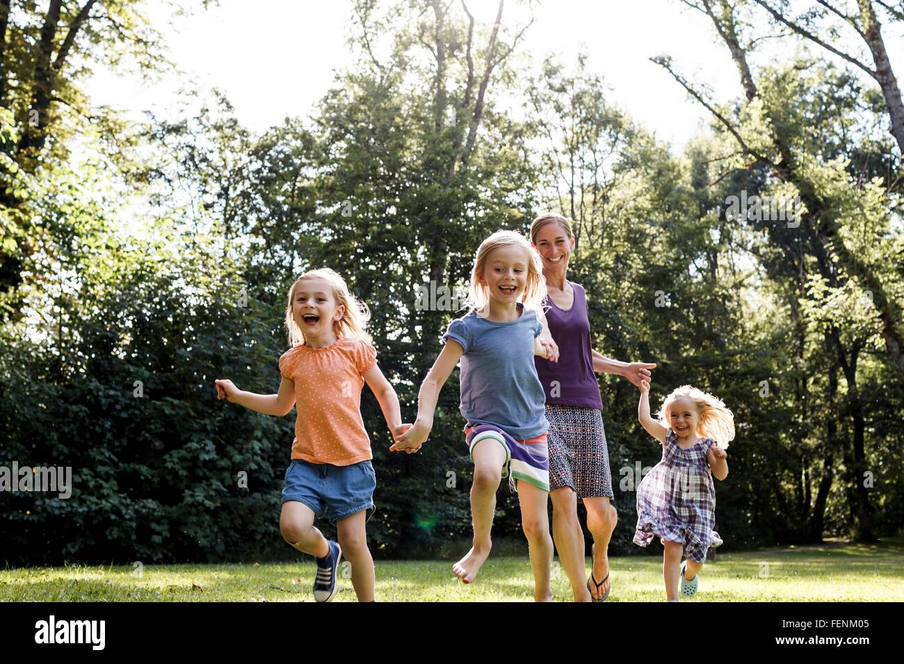 Mid adult woman and three young daughters running in park Stock Photo