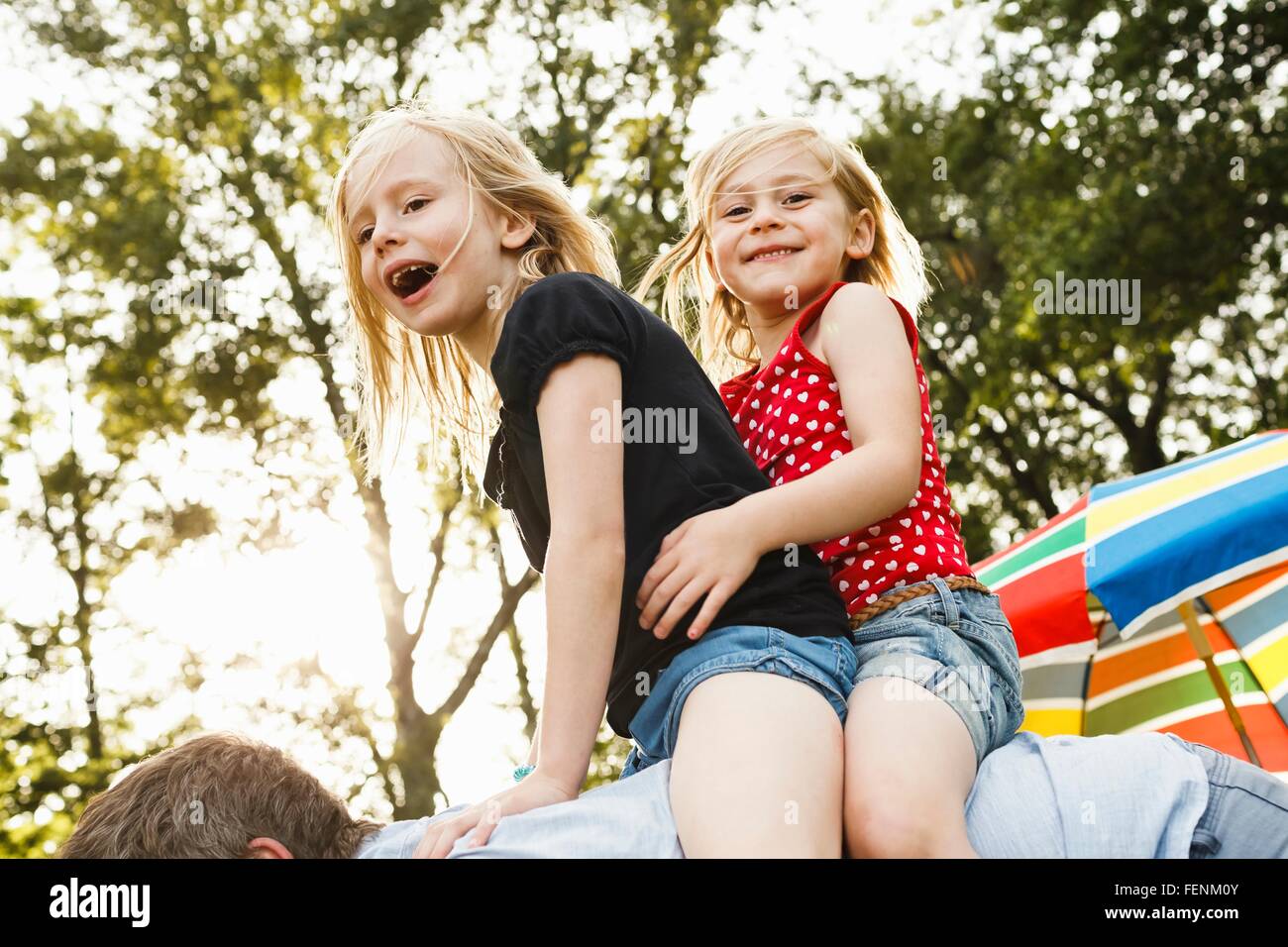 Mature man giving two young daughters piggy back in park Stock Photo