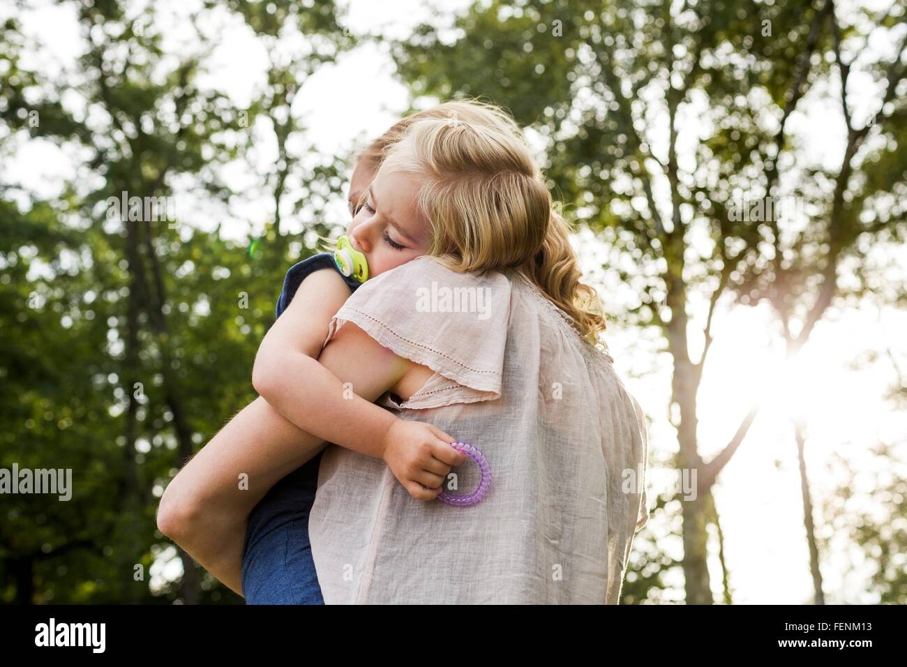 Mid adult woman carrying sleeping daughter in park Stock Photo