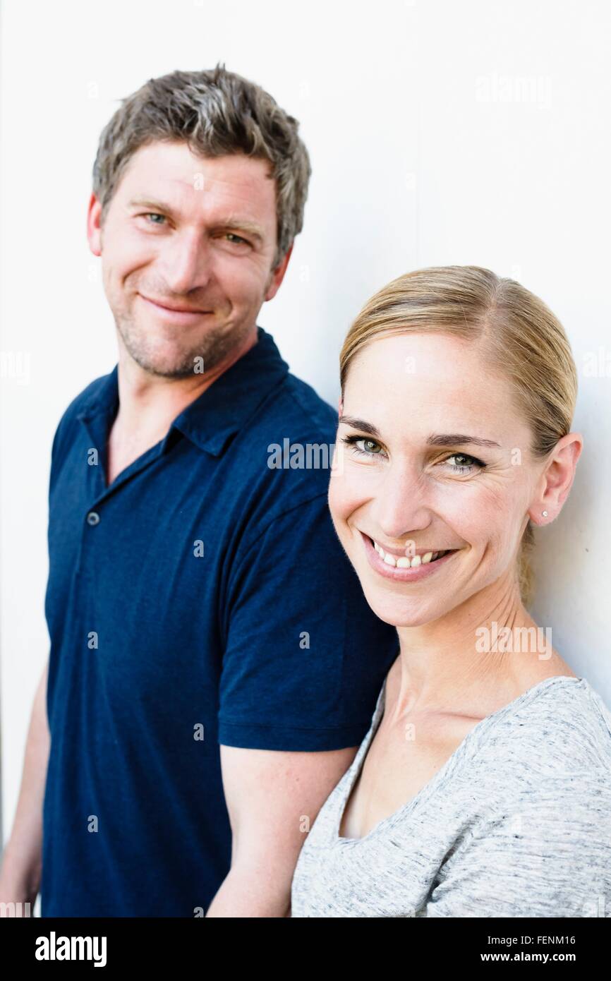 Portrait of mid adult woman and husband leaning against white wall Stock Photo