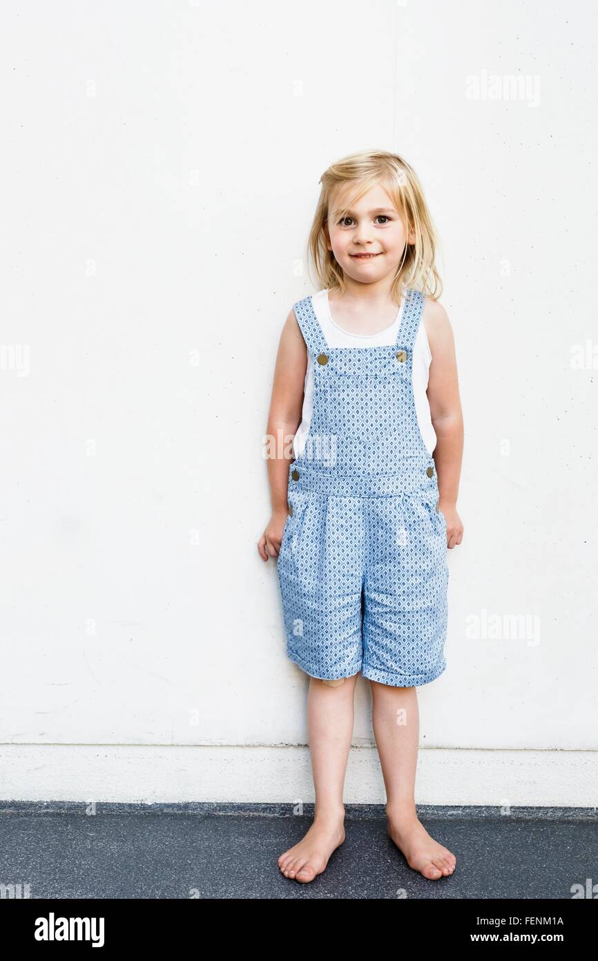 Portrait of girl wearing dungarees in front of white wall Stock Photo