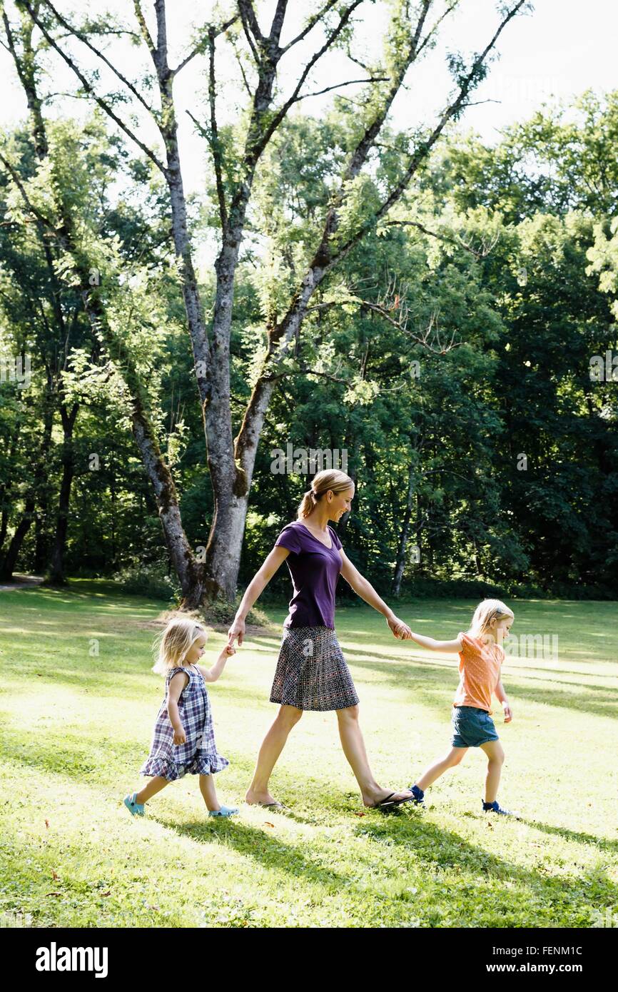 Mid adult woman holding hands with two daughters in park Stock Photo