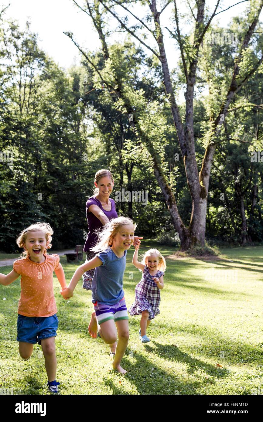 Mid adult woman running and holding hands with three  daughters in park Stock Photo