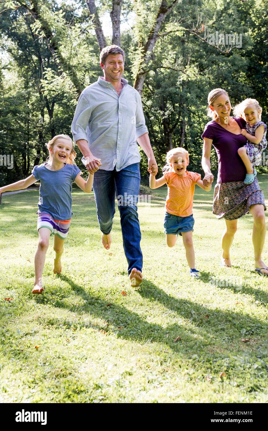 Couple running and holding hands with three  daughters in park Stock Photo