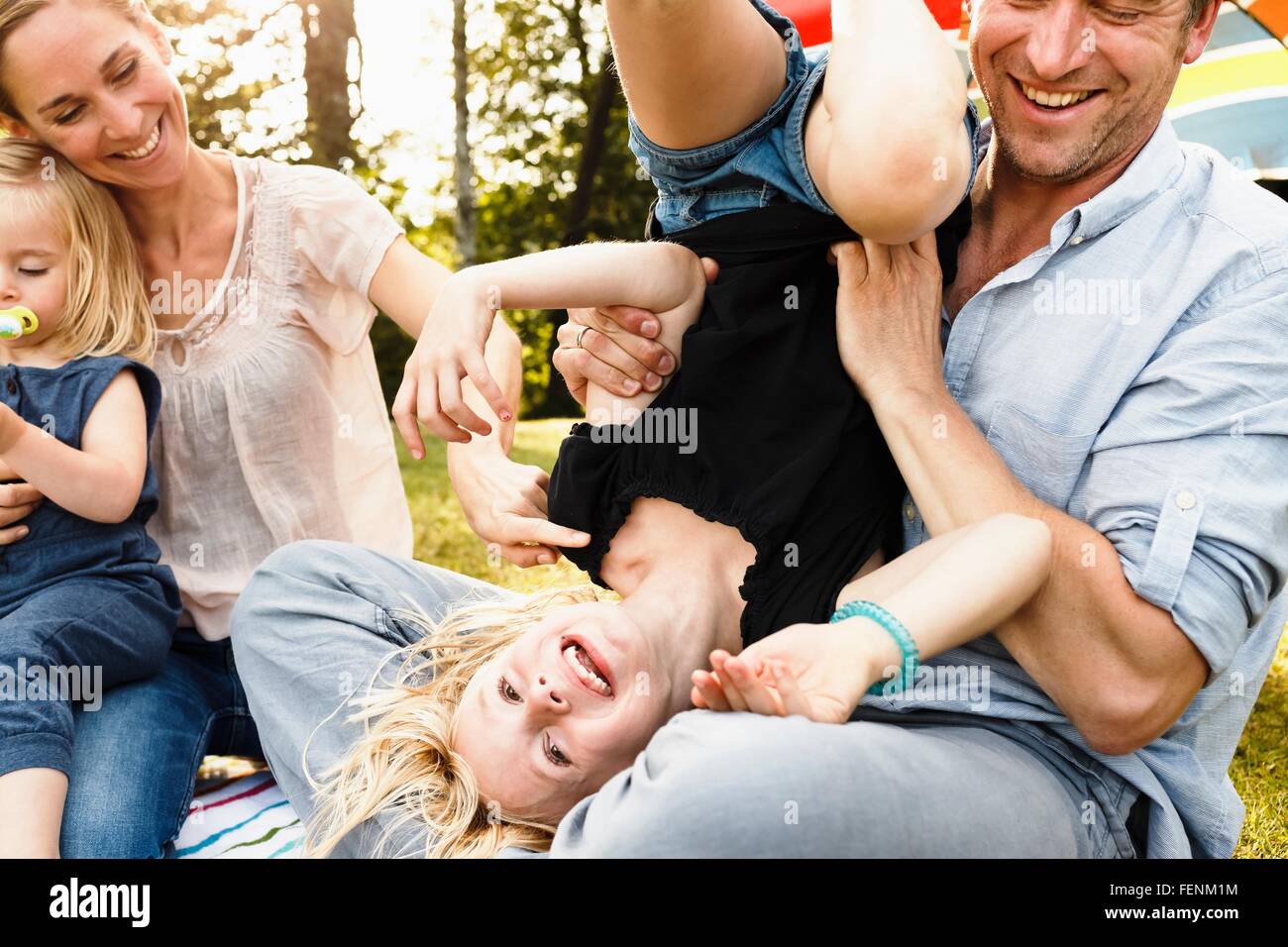 Father turning daughter upside down at family picnic in park Stock Photo