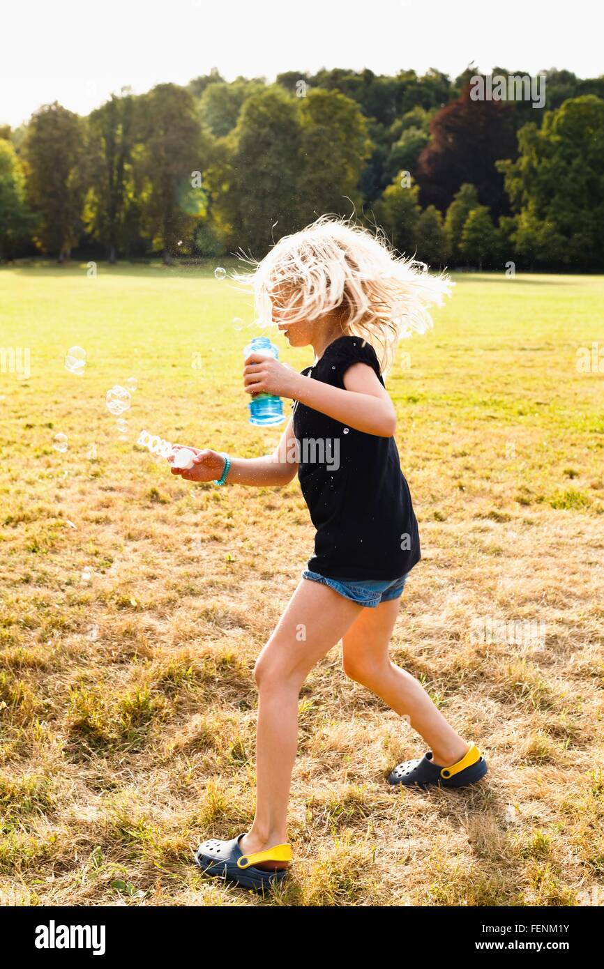 Girl waving bubble wand and making bubbles in park Stock Photo