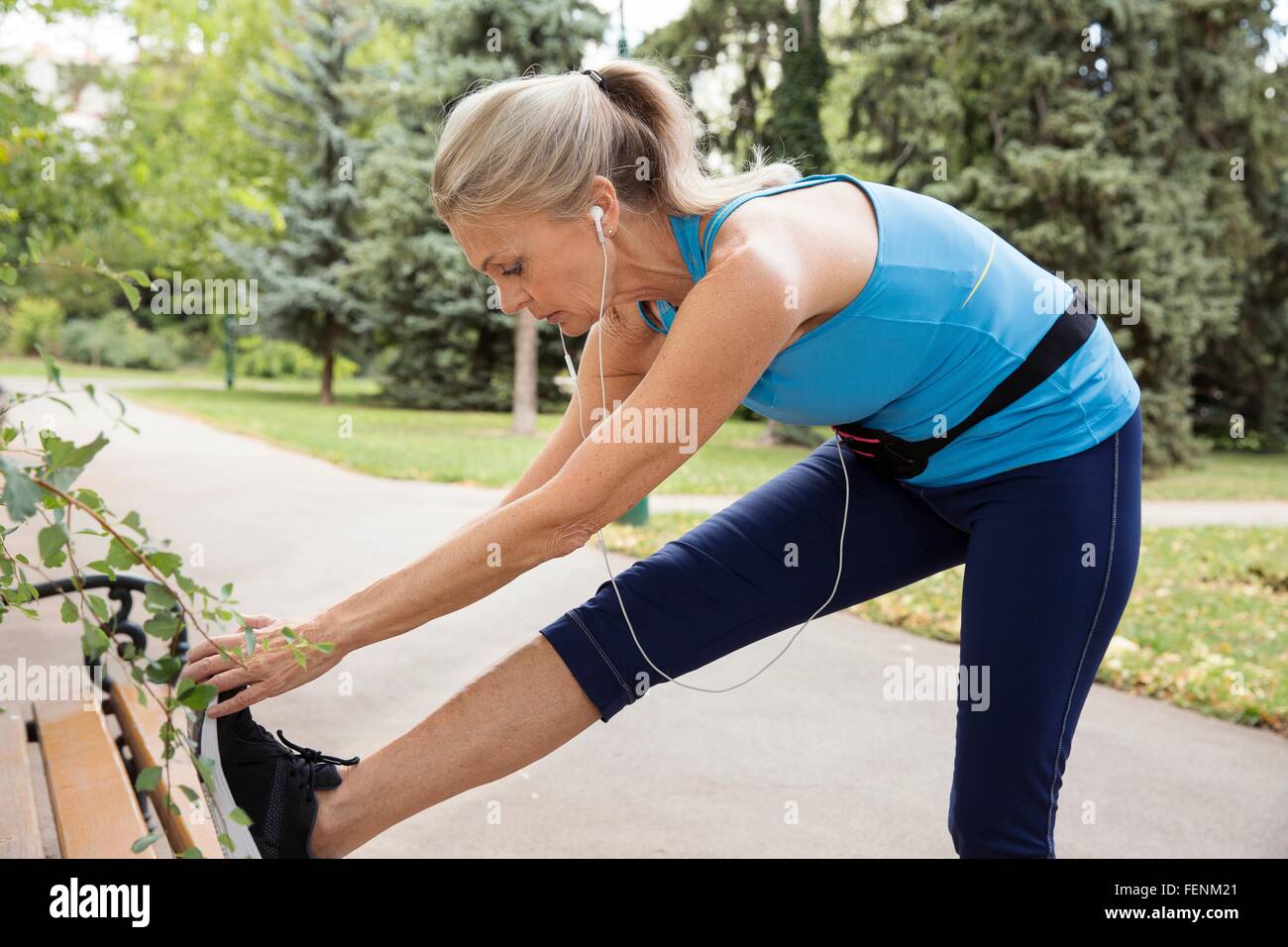 Mature woman training and touching toes on park bench Stock Photo