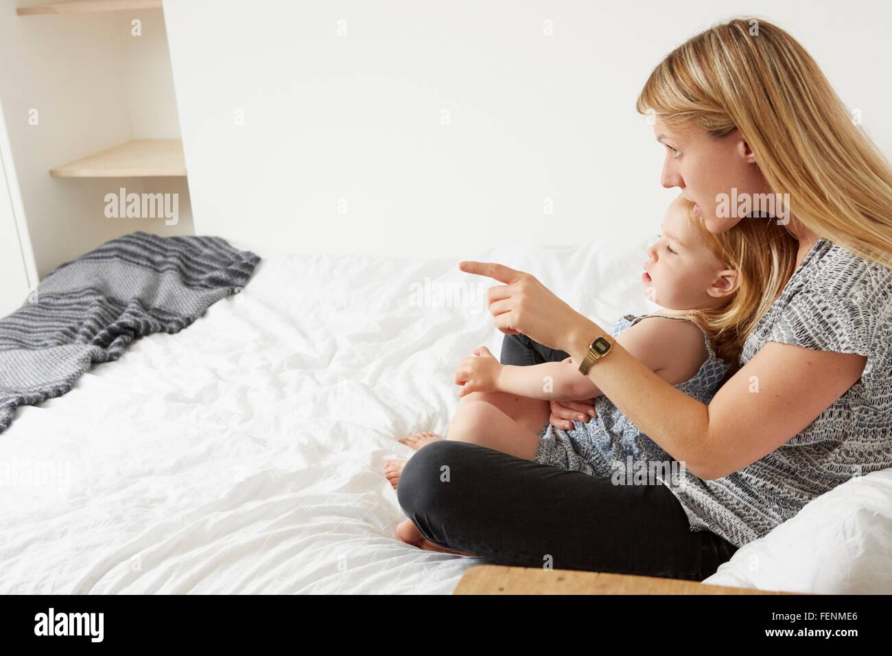 Mid adult woman sitting with toddler daughter on bed Stock Photo