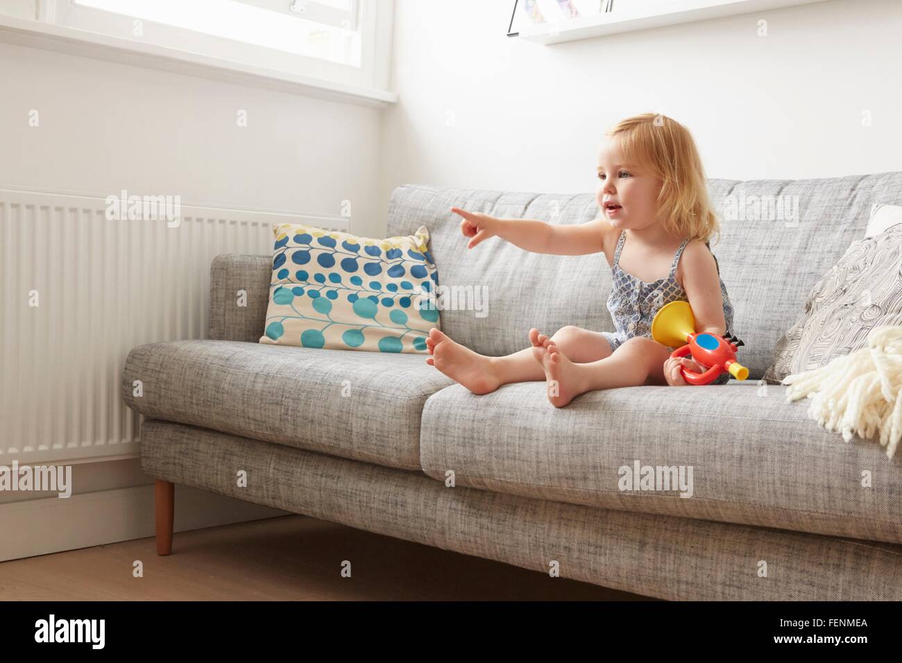 Female toddler playing with toy trumpet on sofa Stock Photo