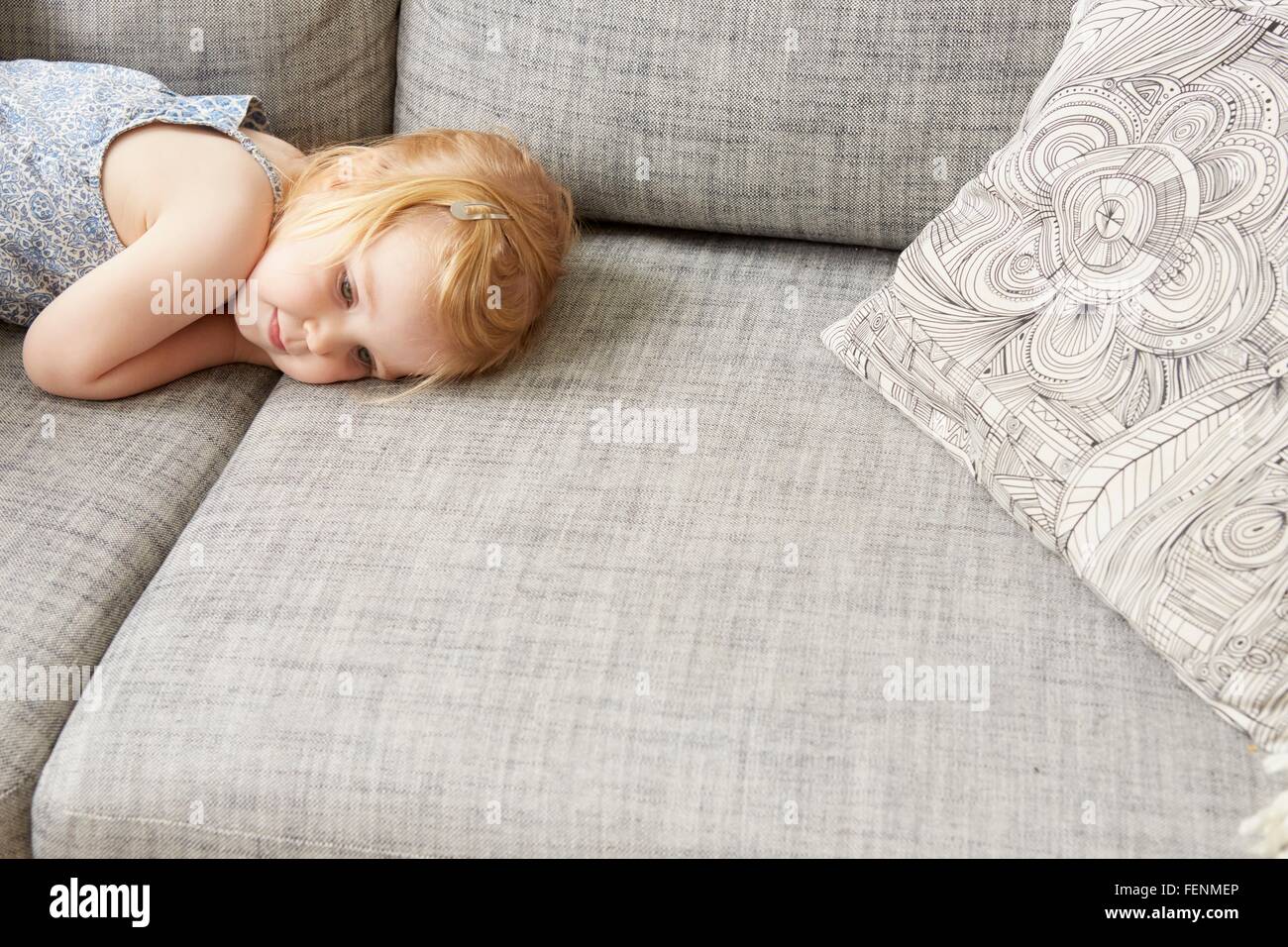Tired female toddler lying on sofa Stock Photo