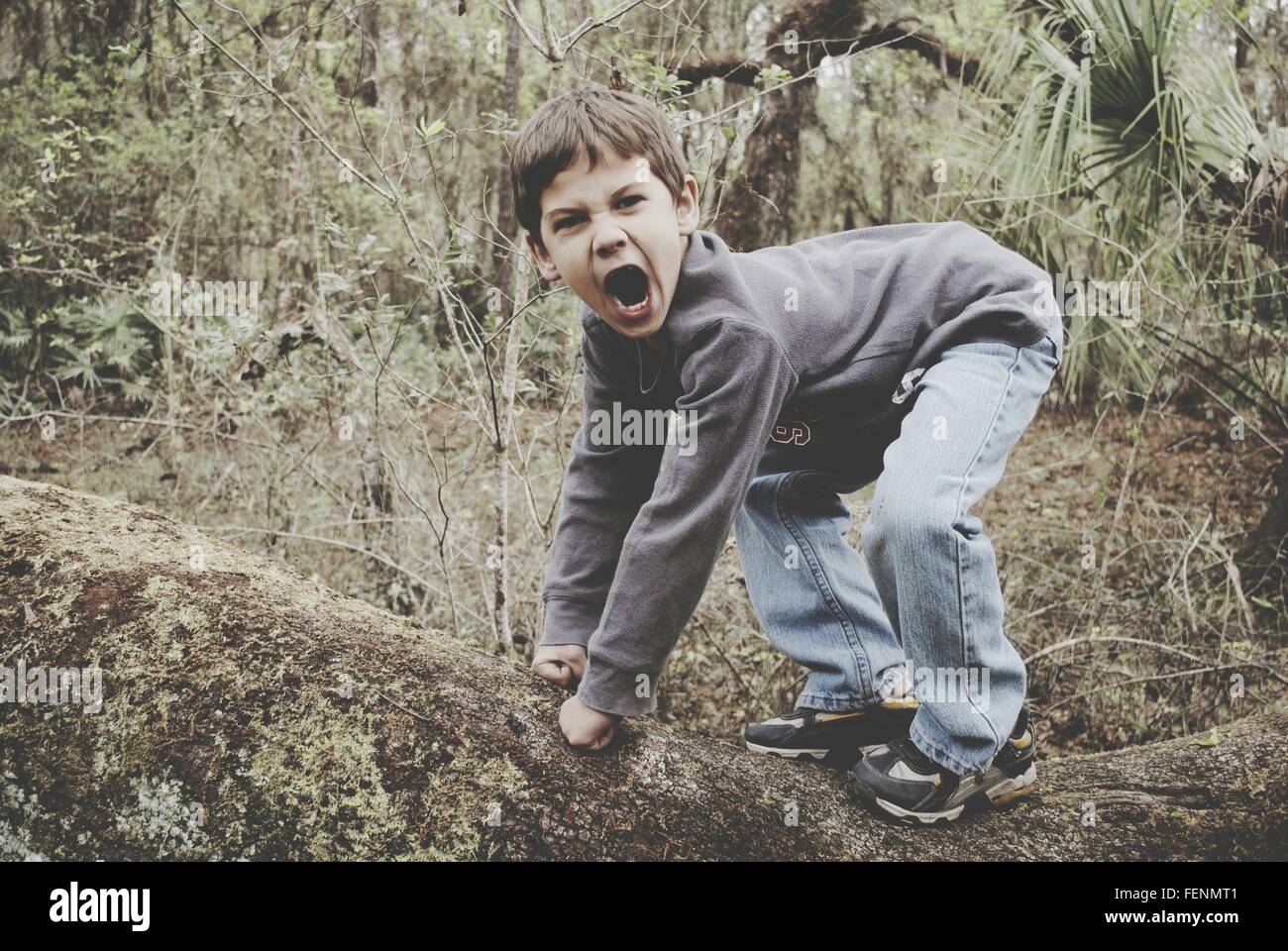 Full Length Side View Of Boy Imitating Gorilla In Forest Stock Photo