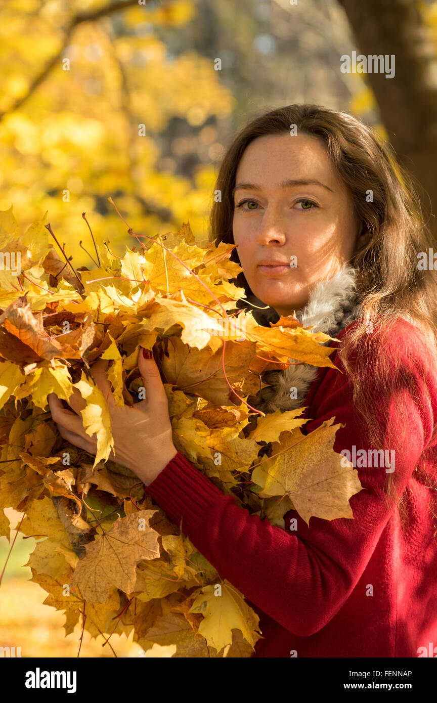 Woman with brown hair at autumn forest holding a yellow maple leafs ...