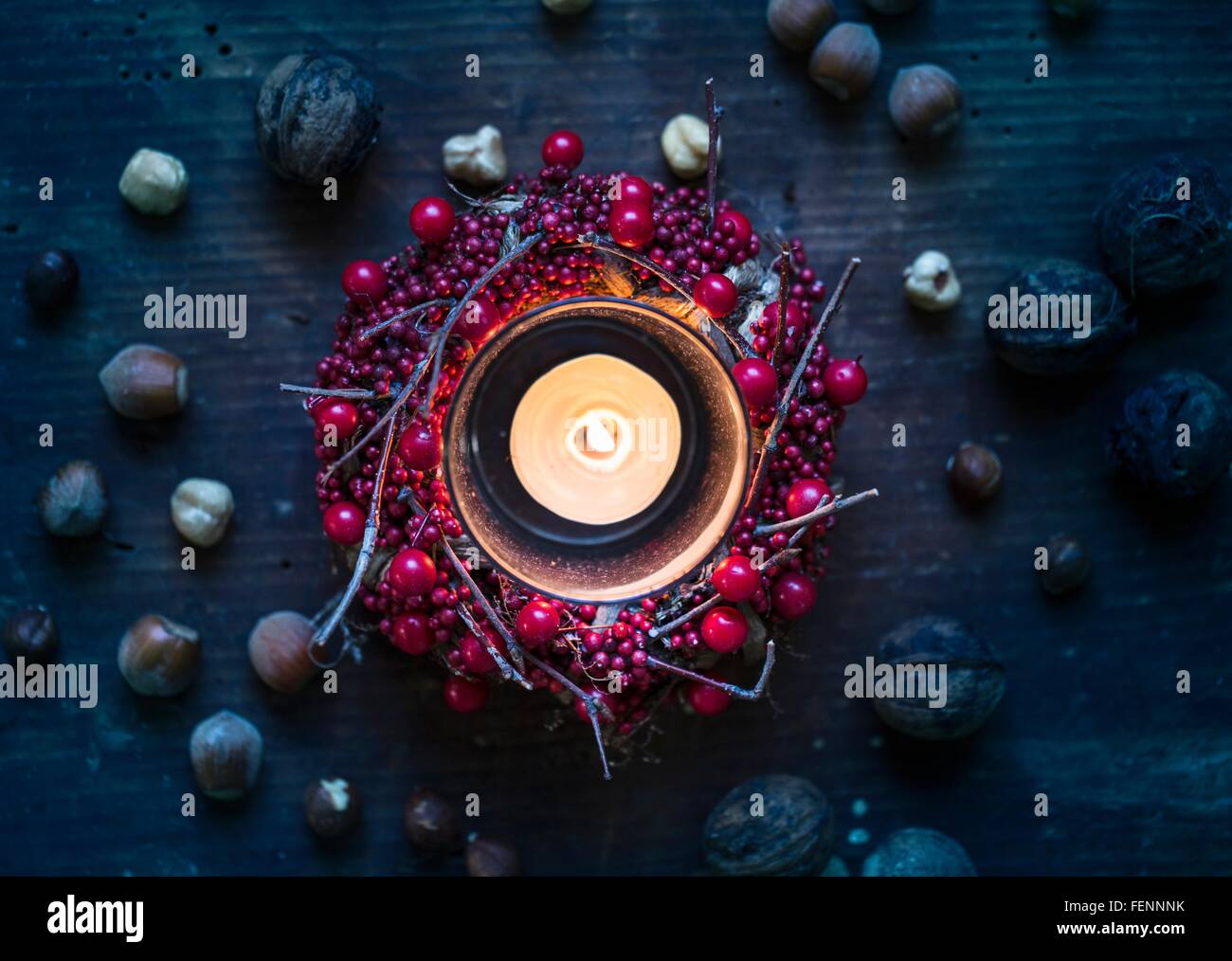 Overhead view of burning candle surrounded by berry wreath and nuts Stock Photo