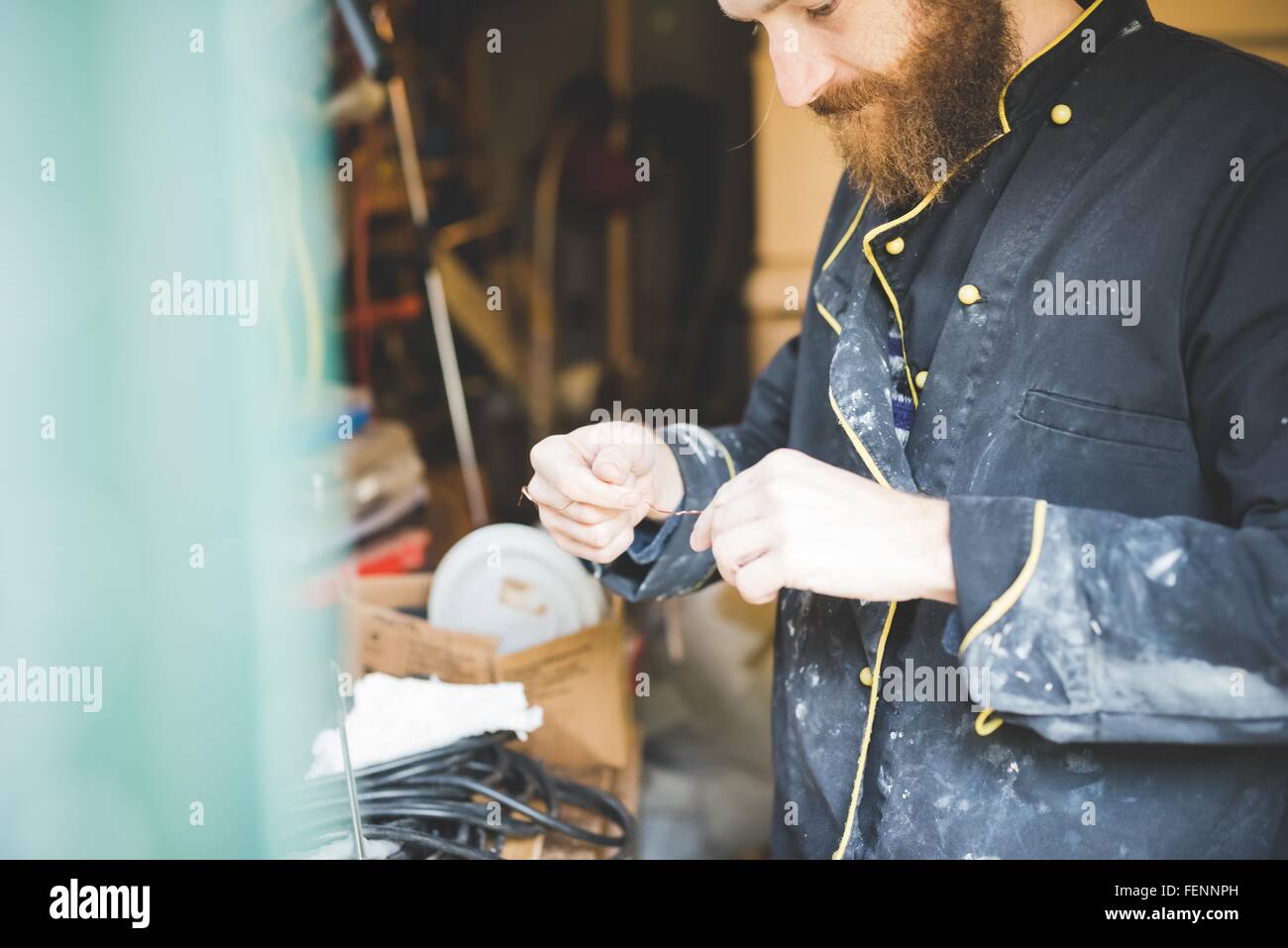Bearded man in workshop holding wire looking down Stock Photo