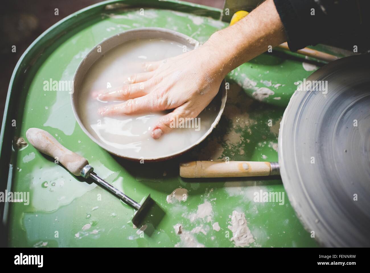 Mid adult mans hand immersed in bowl of water on pottery wheel Stock Photo