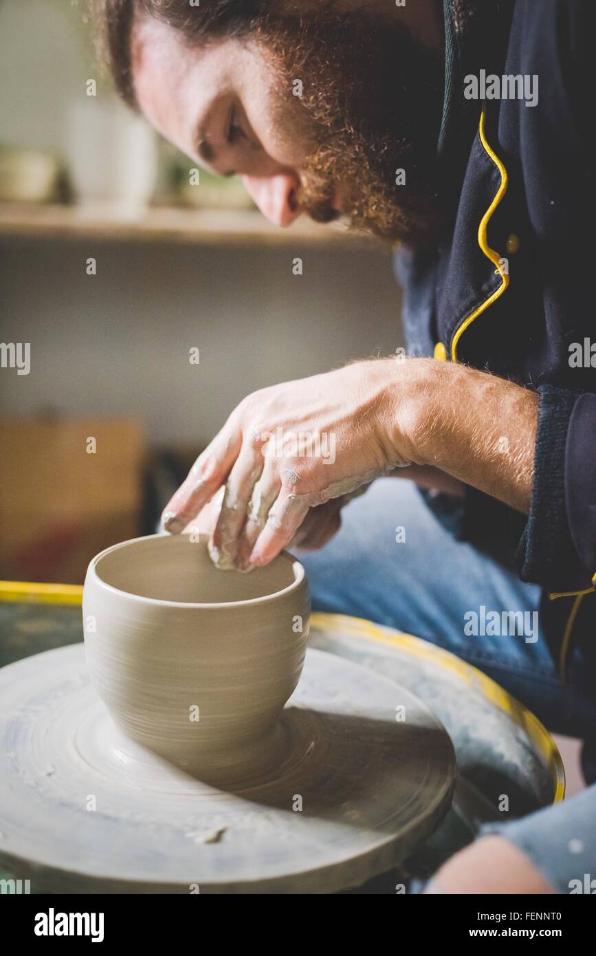 Side view of bearded mid adult man looking down, making clay pot on pottery wheel Stock Photo