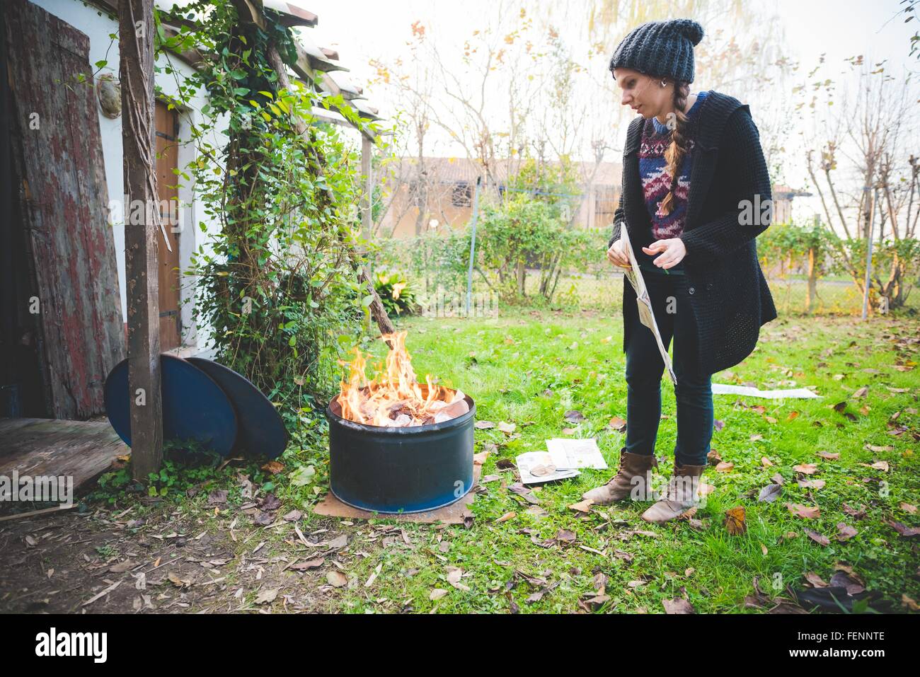 Side view of young woman wearing knit hat by fire in metal barrel Stock Photo