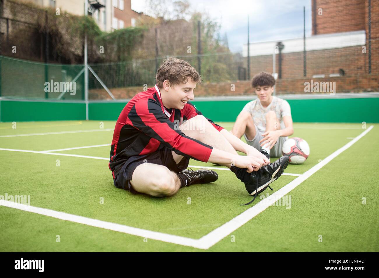 Two young men on urban football pitch, tying shoelaces Stock Photo
