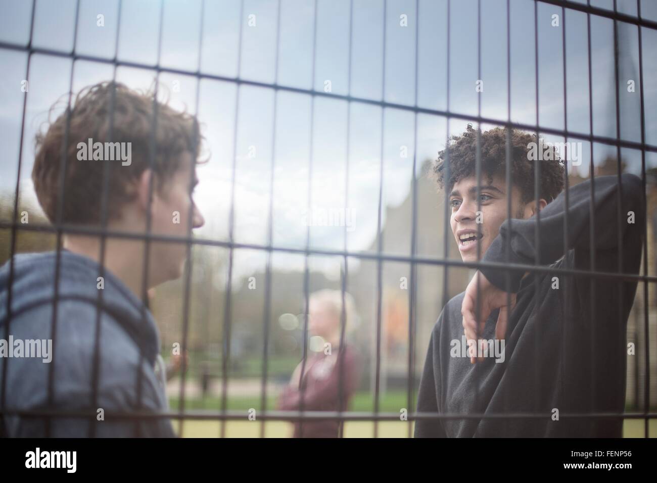 Two young men leaning against fence, talking Stock Photo