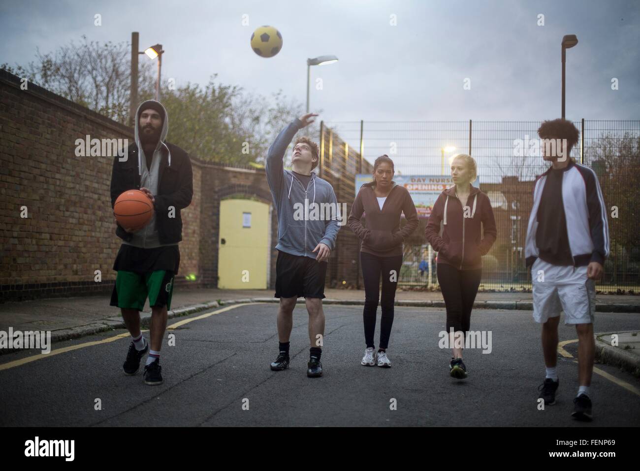 Group of adults walking in road, holding basketball and football Stock Photo