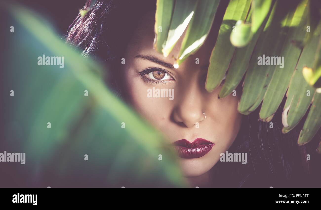 Portrait of beautiful sultry young woman behind leaves at night Stock Photo