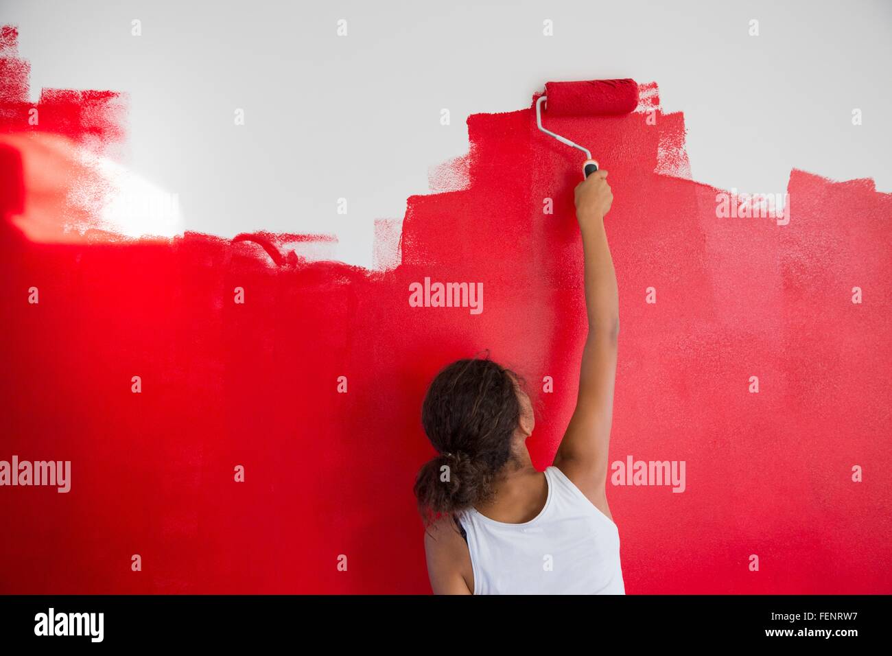 Rear View Of Girl Painting Red Wall With Paint Roller Stock Photo