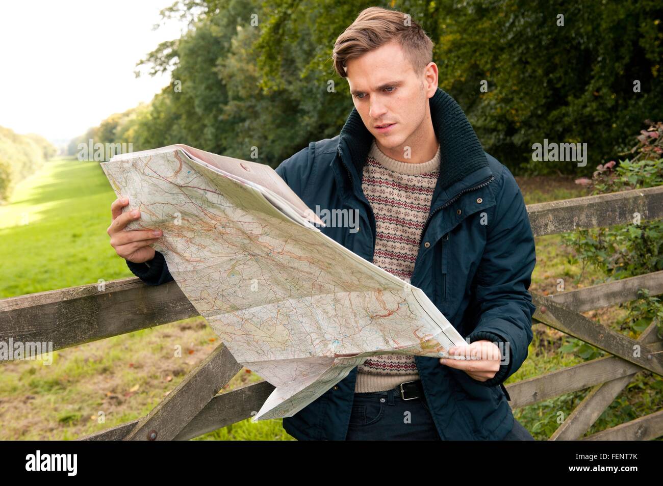 Young man leaning against rural gate reading map Stock Photo