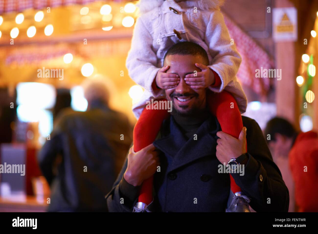 Father carrying daughter on shoulders, daughter covering father's eyes Stock Photo