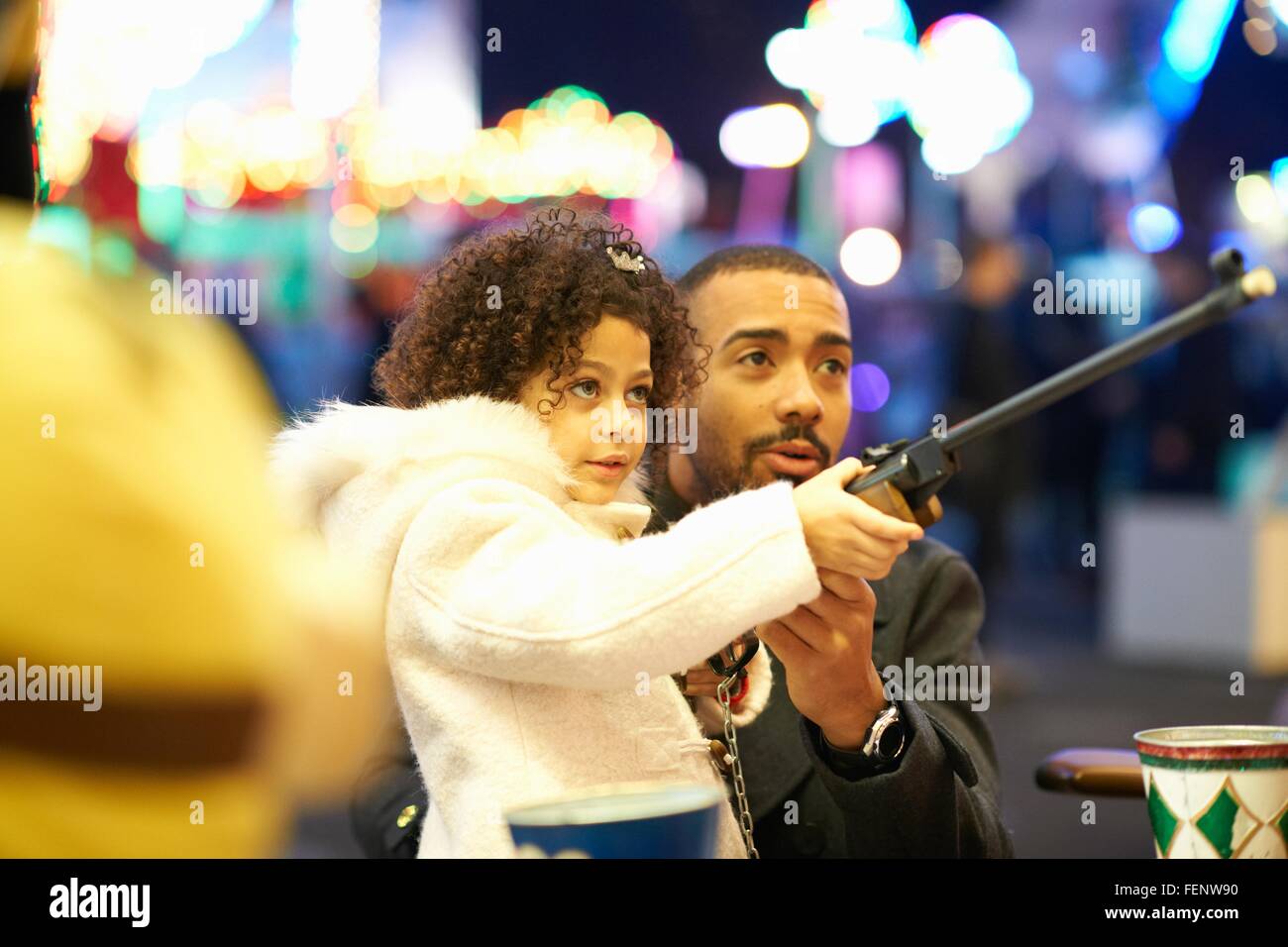 Father helping daughter with rifle at shooting gallery at funfair Stock Photo