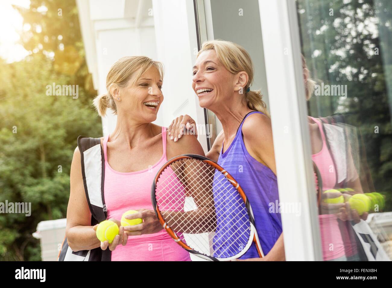 Two mature women preparing to play tennis at patio door Stock Photo