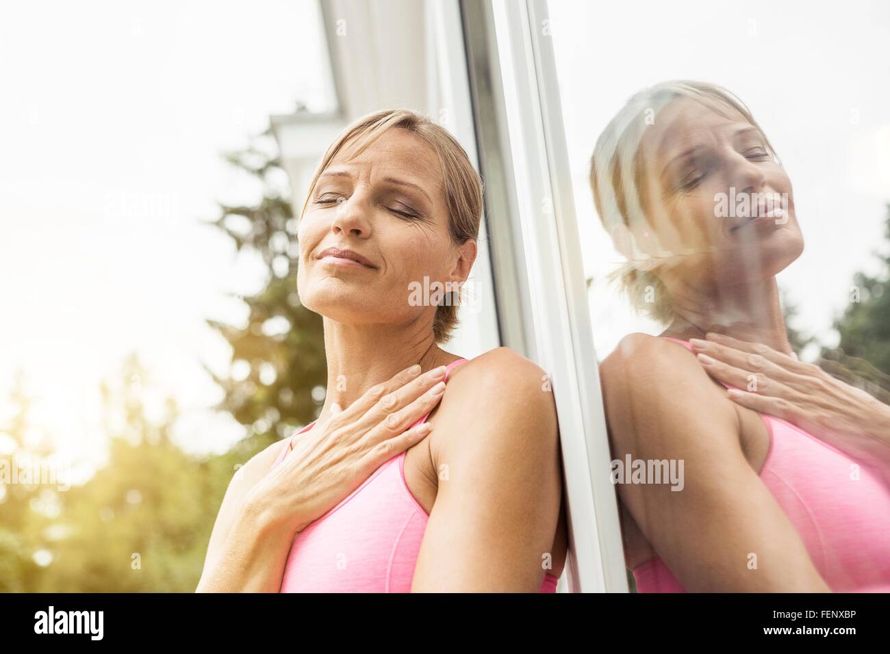 Exhausted mature female runner leaning against patio door Stock Photo