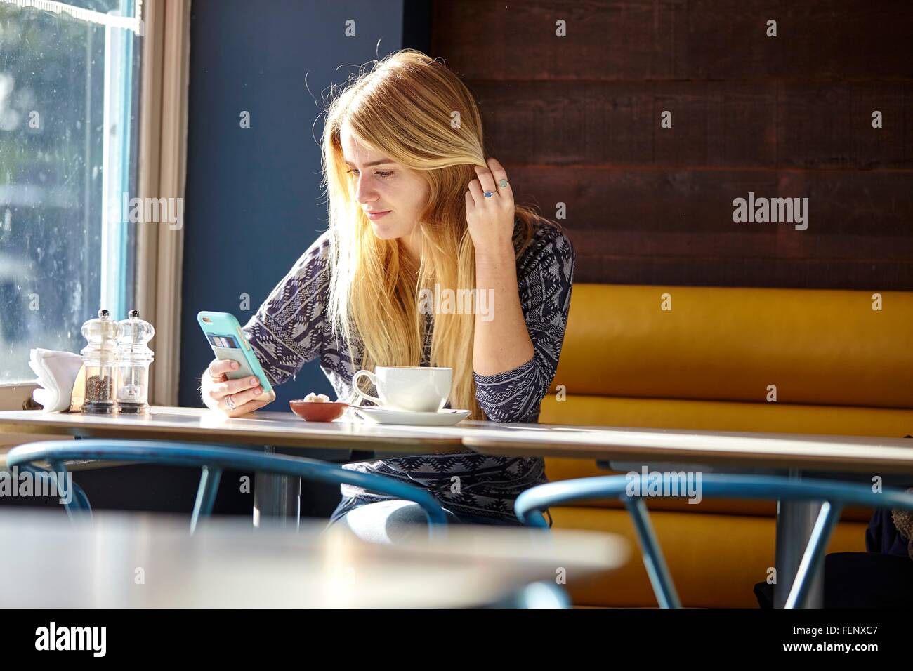 Young woman alone in cafe reading smartphone texts Stock Photo