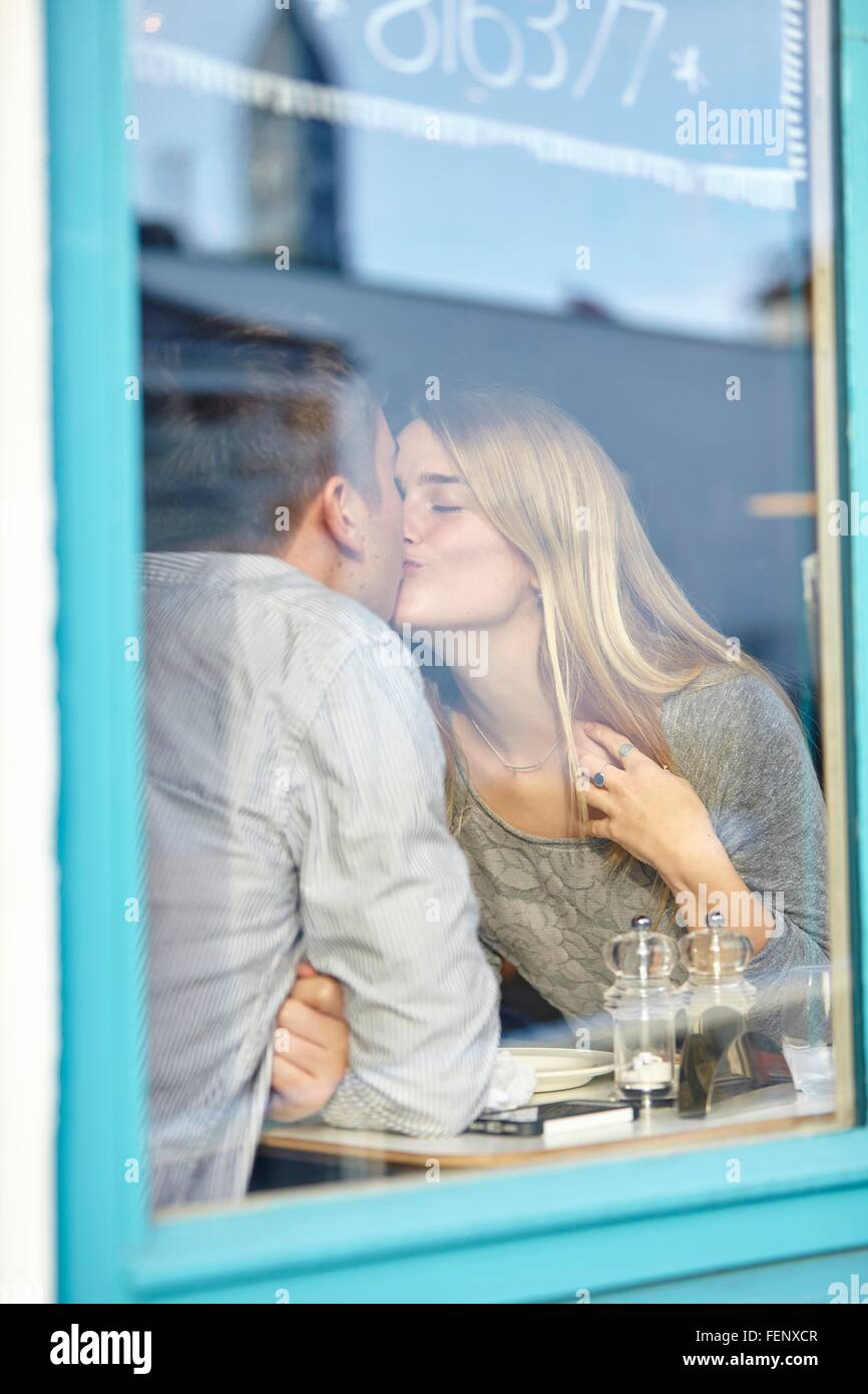 Romantic young couple at cafe window kissing Stock Photo
