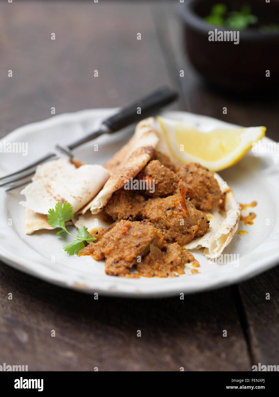 Plate of Goan pork dish with naan bread, lemon slice, coriander and chilli Stock Photo