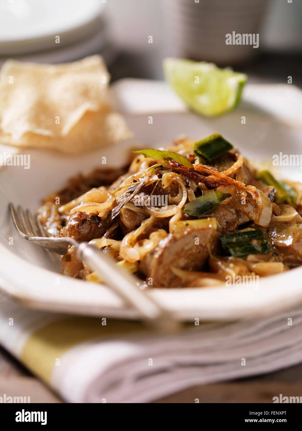 Bowl of black lamb curry with onions, lime slice and papadums Stock Photo