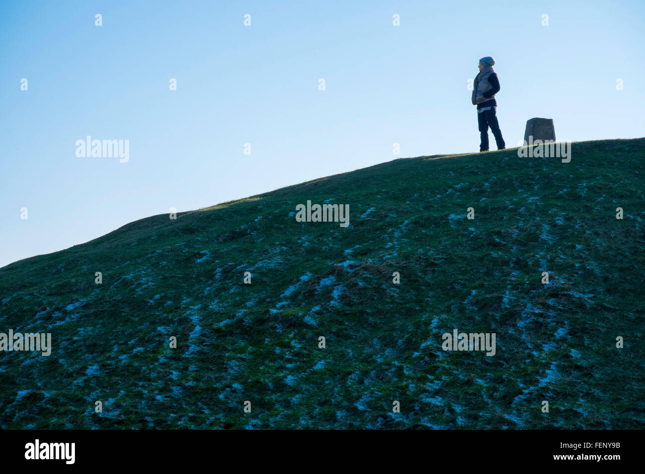 Woman standing close to a triangulation pillar, on top of ancient burial mound, situated on the summit of Garth Mountain, north Stock Photo
