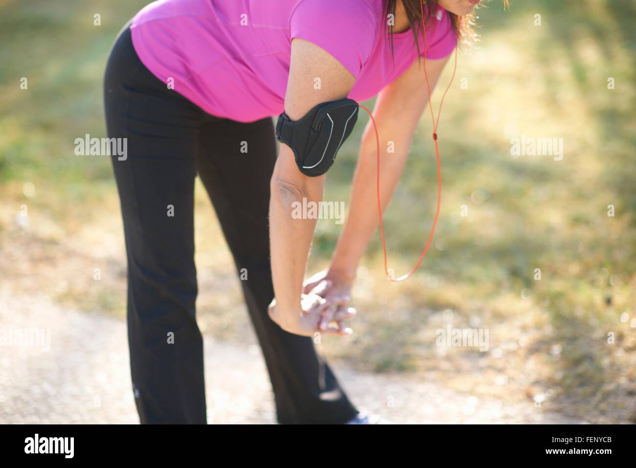 Neck down of mature woman wearing wristband, hands together bending over stretching Stock Photo