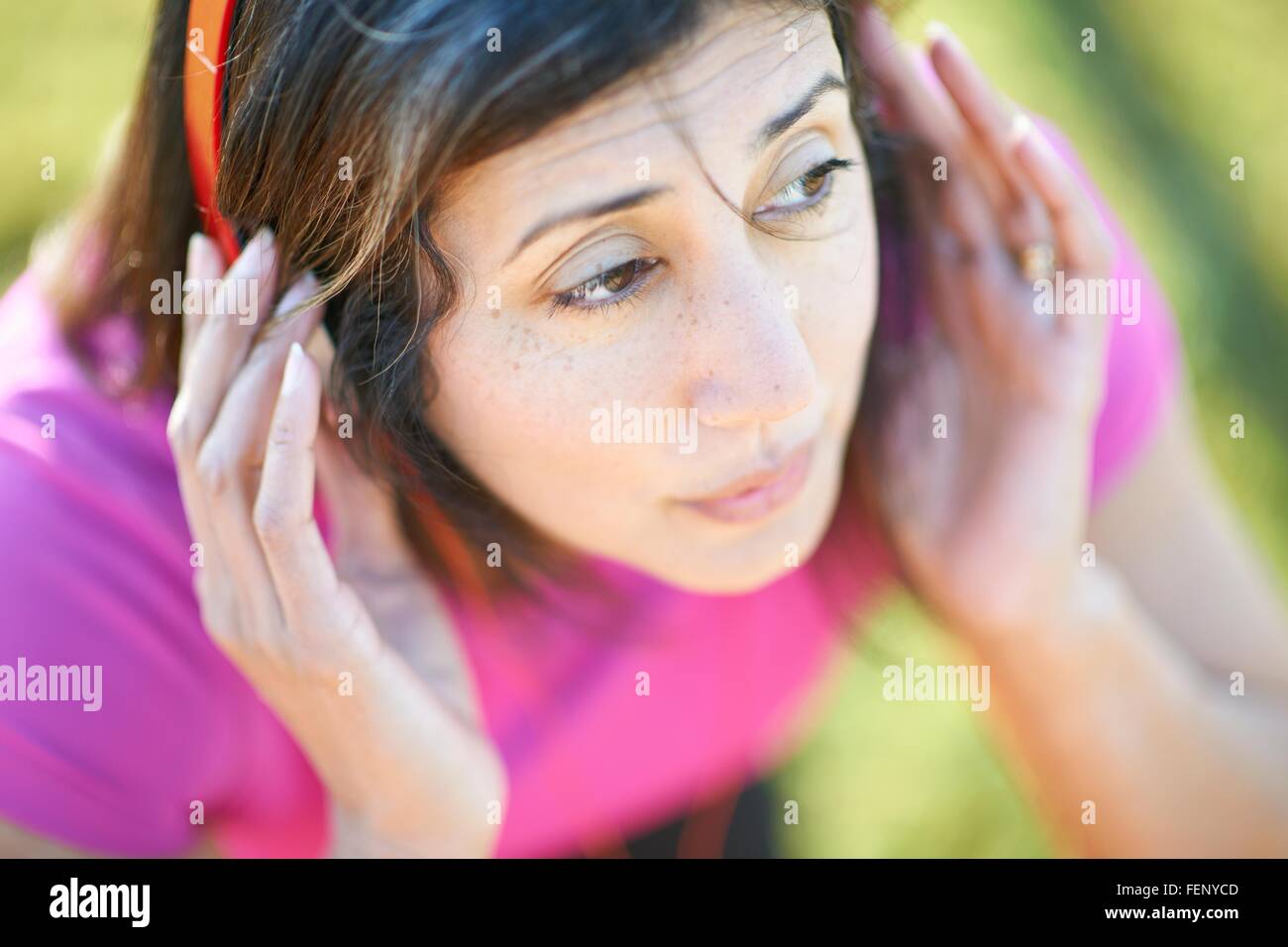 Cropped high angle view of mature woman wearing headphones, hands on ears looking away Stock Photo