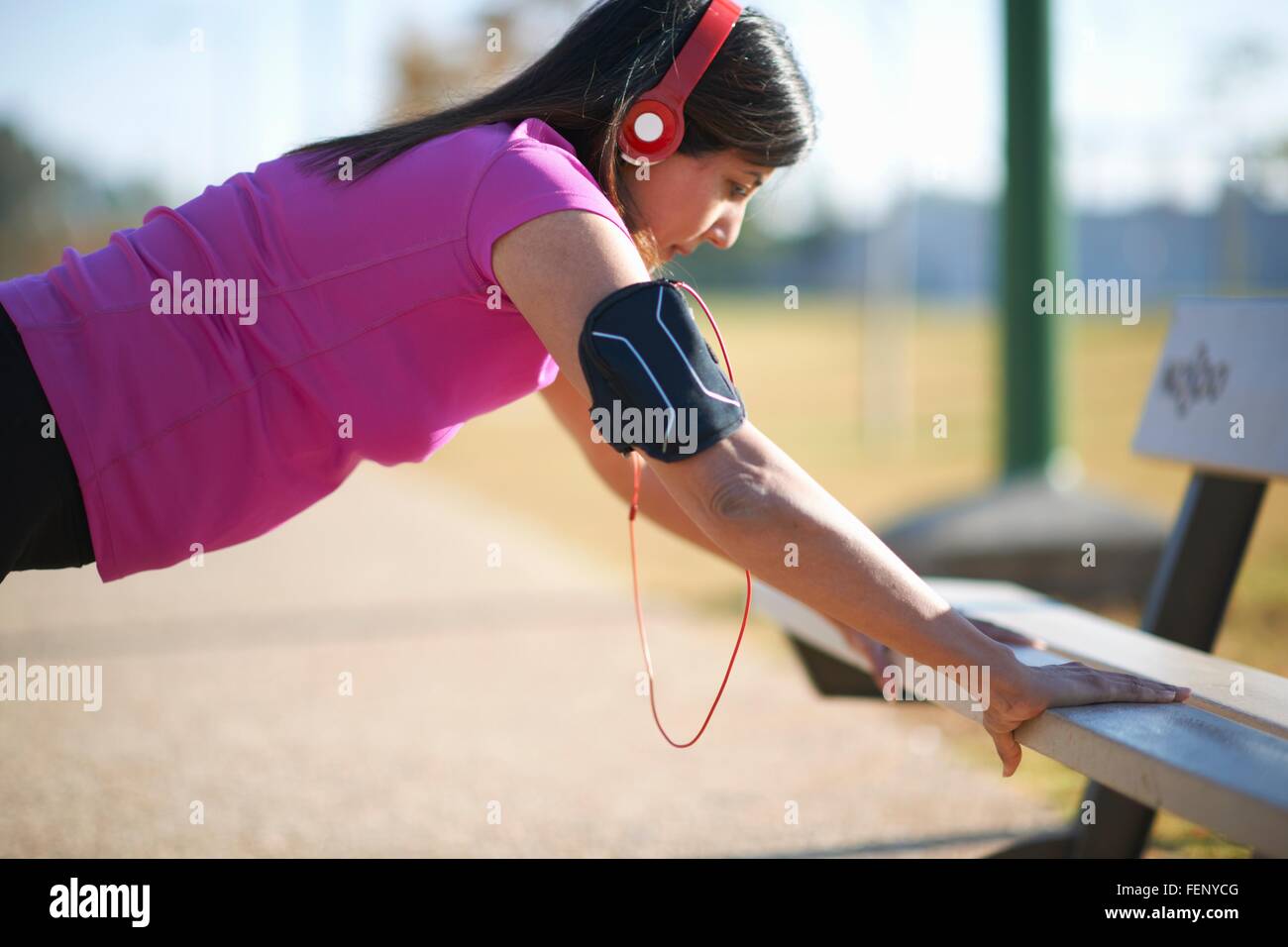 Side view of mature woman wearing headphones doing push up using park bench Stock Photo