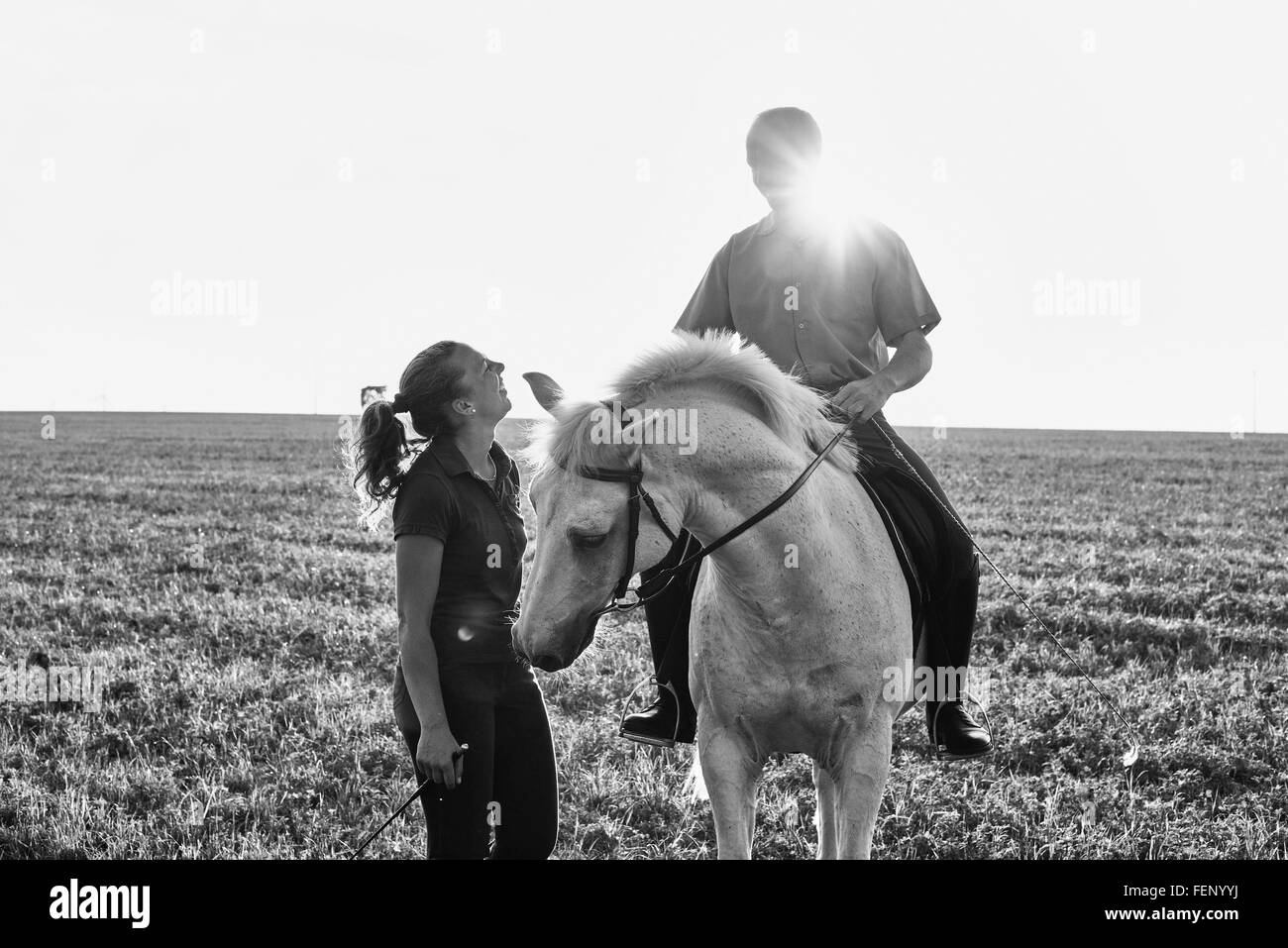 B&W image of woman chatting with man riding grey horse in field Stock Photo