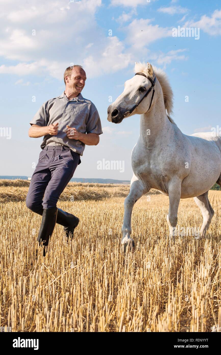 Male trainer running in front of white horse in field Stock Photo