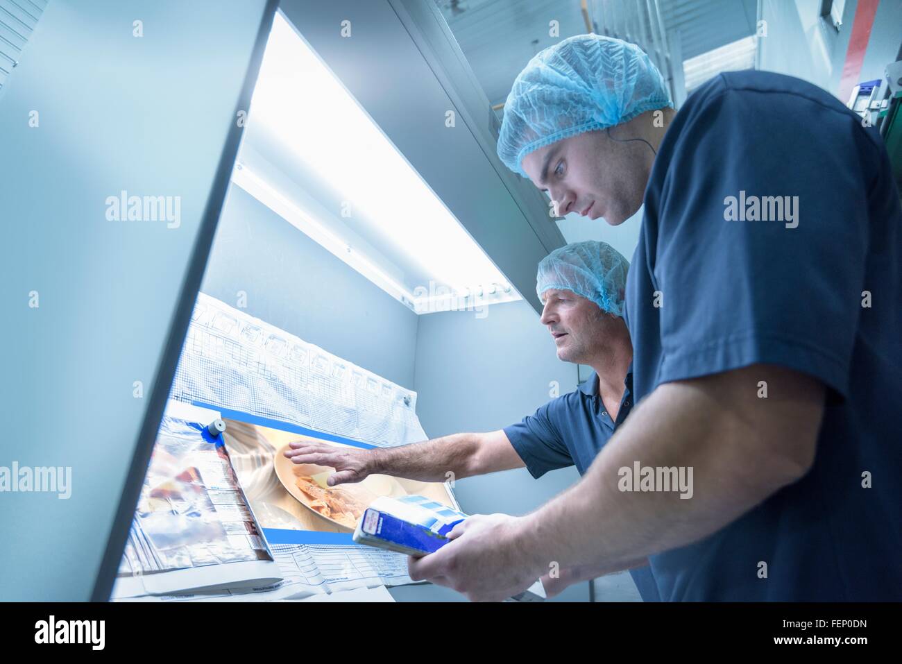 Workers inspecting printed material in food packaging printing factory ...