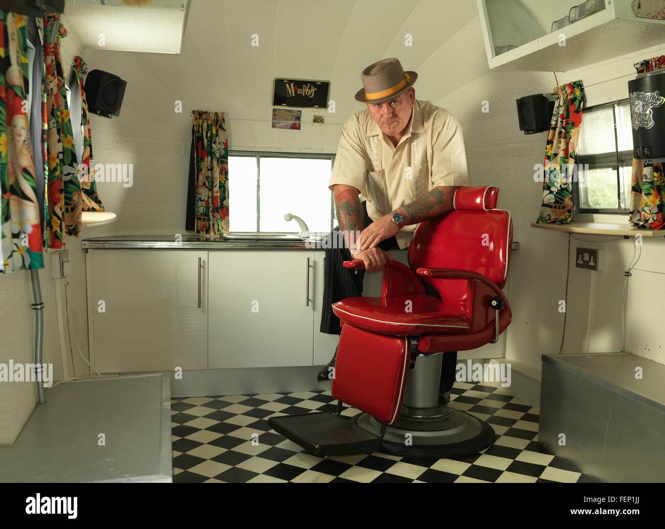 Tattoo artist in mobile tattoo parlour wearing pork pie hat looking at