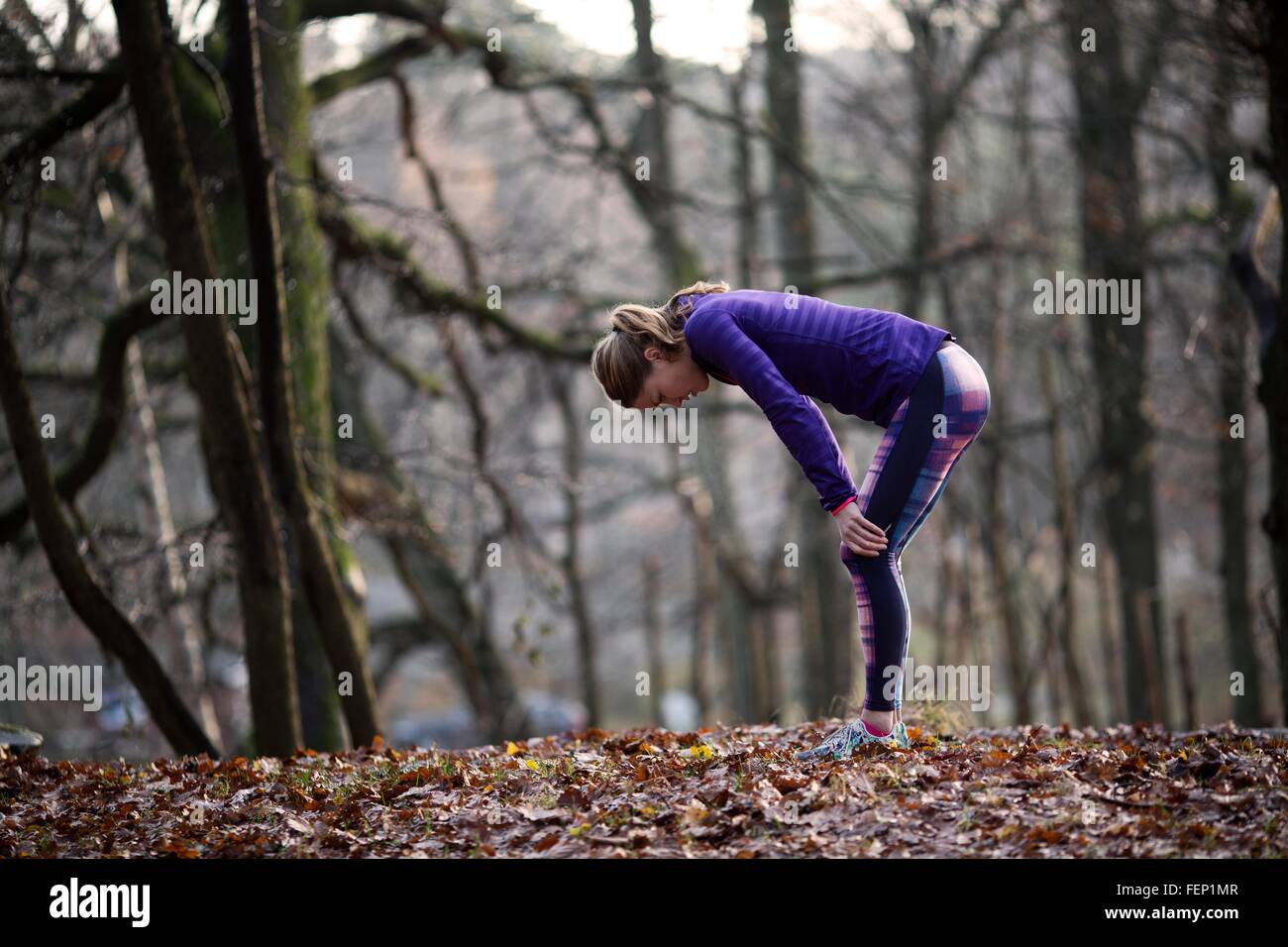 Side view of young woman wearing sports clothing bending over hands on knees, exhausted Stock Photo